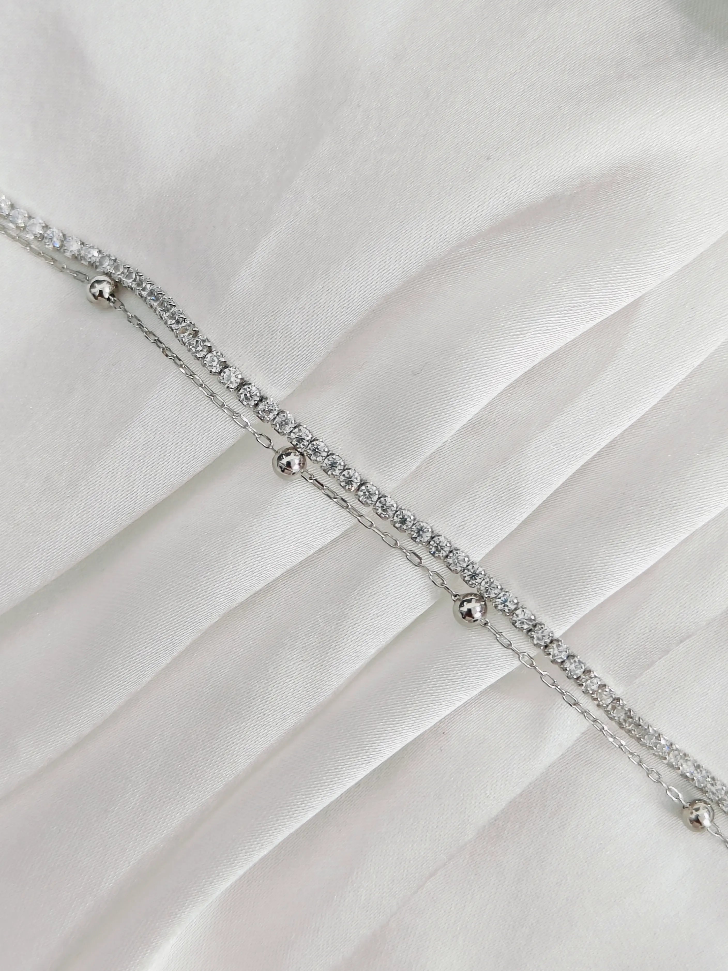 Silver bracelet with small beads on a white fabric background